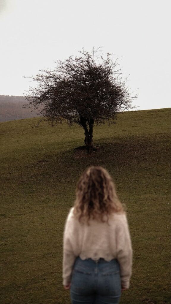 Woman standing alone gazing at a tree in autumn, representing self-awareness in recovery