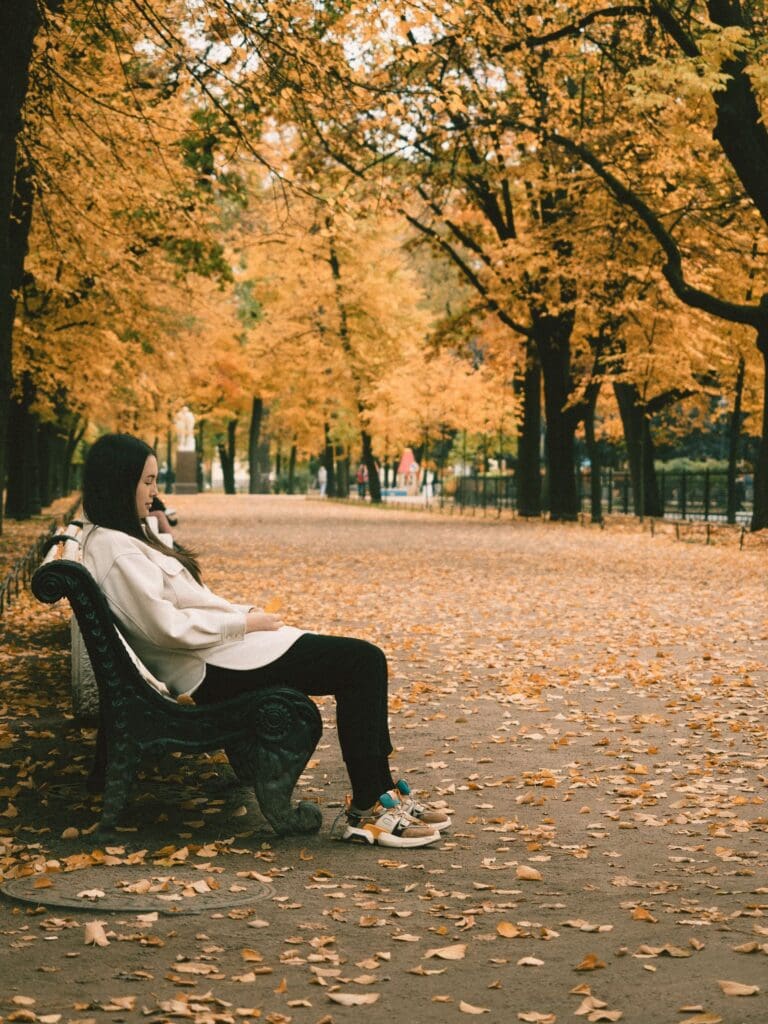 Woman sitting quietly on a park bench in autumn, representing rest and self-awareness in recovery