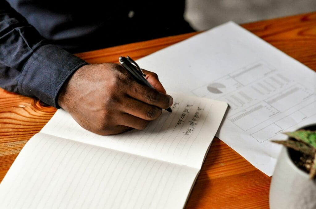 Hand holding a pen, writing in a notebook