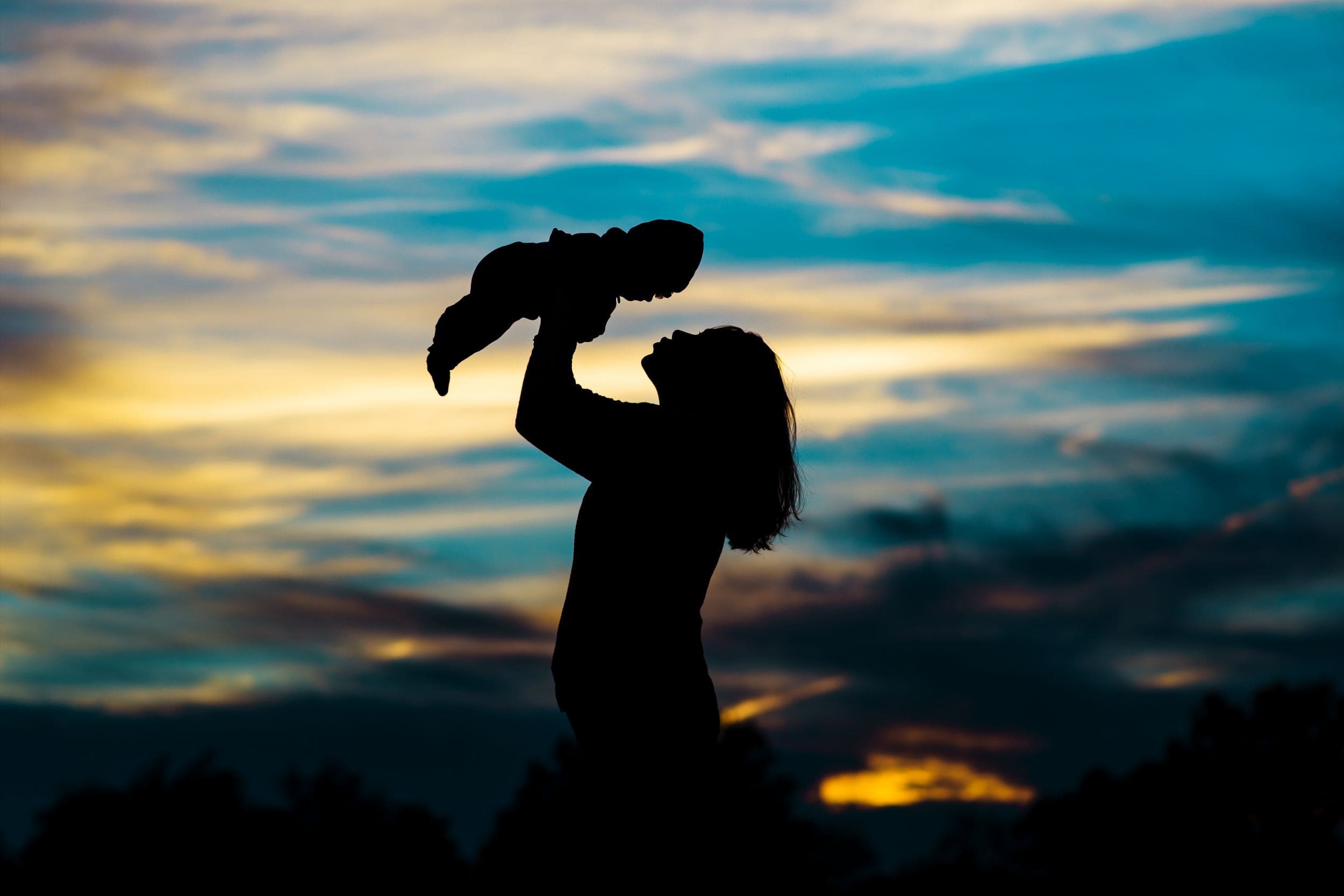 Woman holding baby up in front of the sky