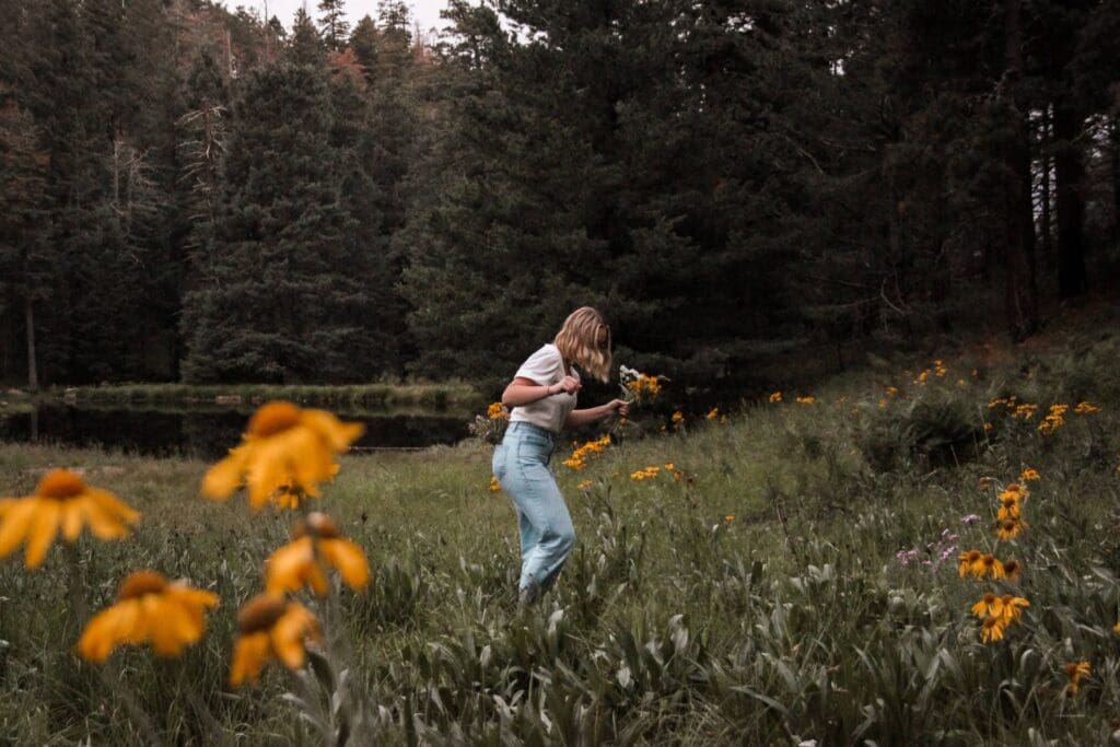 Woman walking alone through a wildflower field surrounded by forest, moving forward with quiet resolve