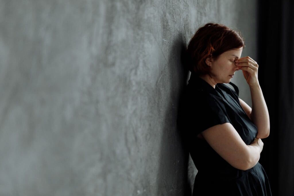 Woman leaning against a concrete wall with eyes closed, expressing stress and emotional exhaustion