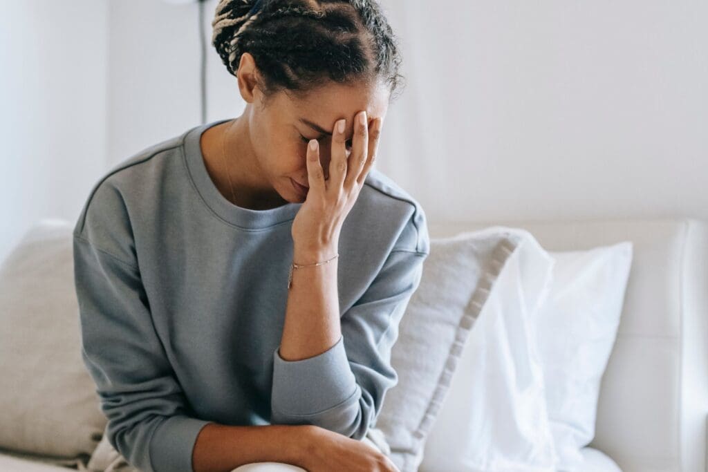 Woman sitting on a bed with her face in her hands, conveying anxiety and emotional overwhelm