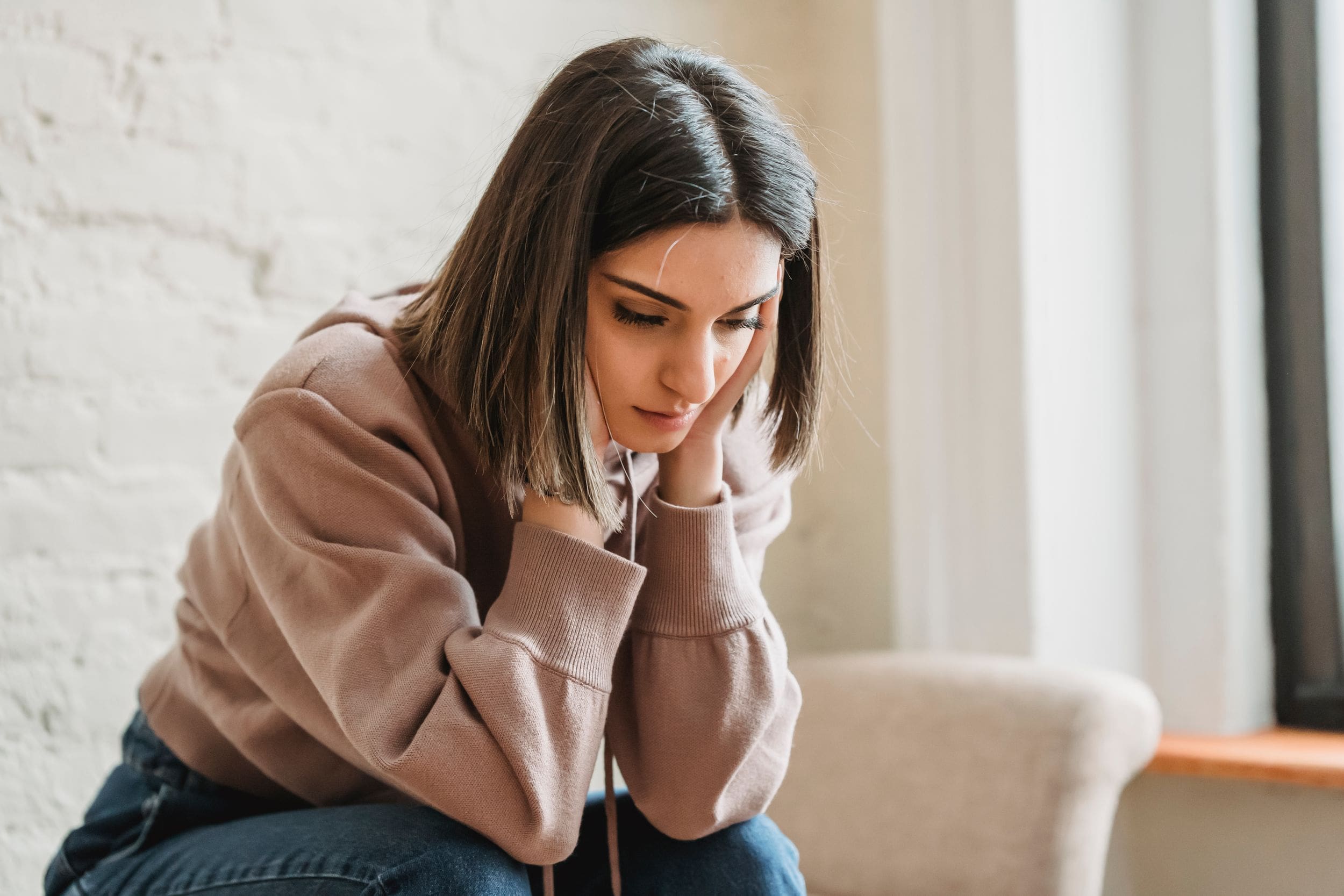 Woman sitting alone on a couch, looking down with a sad and contemplative expression