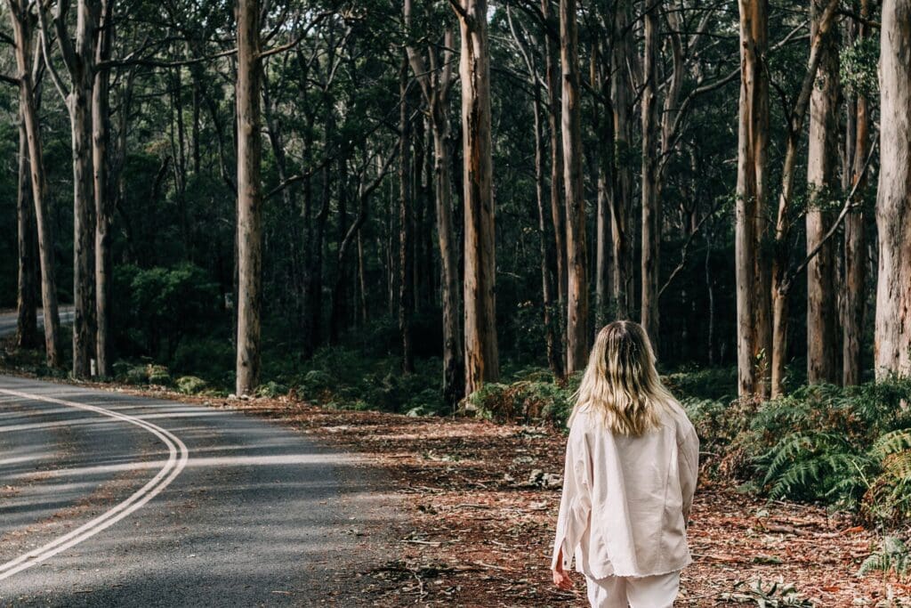 Woman walking alone on a quiet forest road surrounded by autumn trees