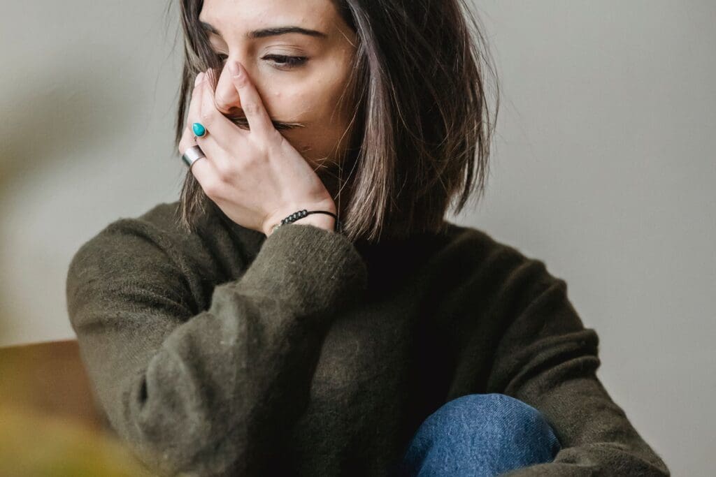 Woman sitting alone in a dimly lit room, conveying emotional exhaustion and quiet distress