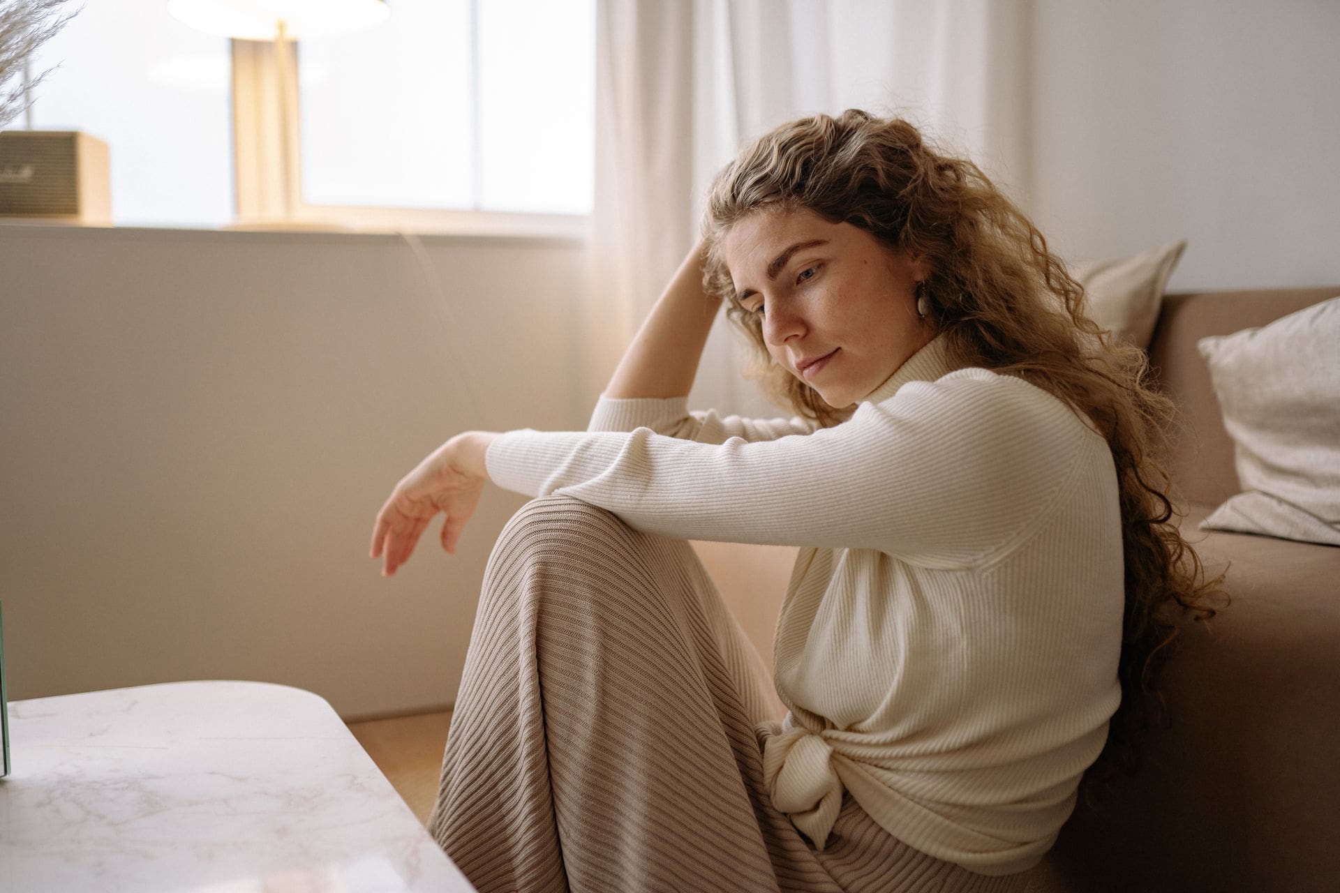 Woman sitting alone in a cozy living room, looking pensive in soft natural light