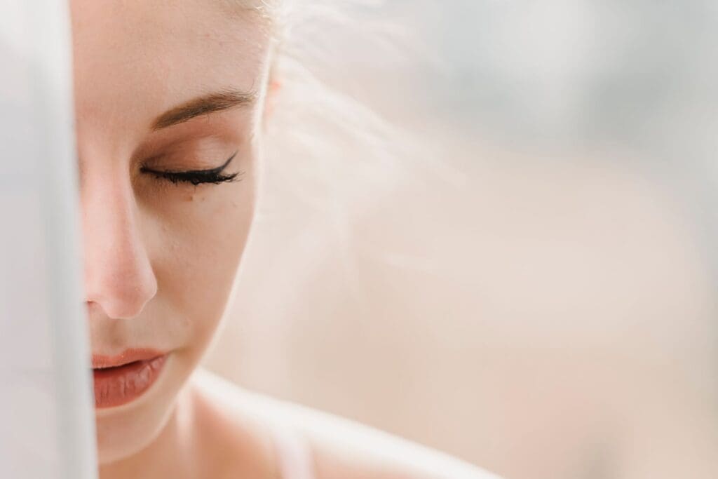 Woman sitting near a sunny window with eyes closed, looking peaceful and grounded