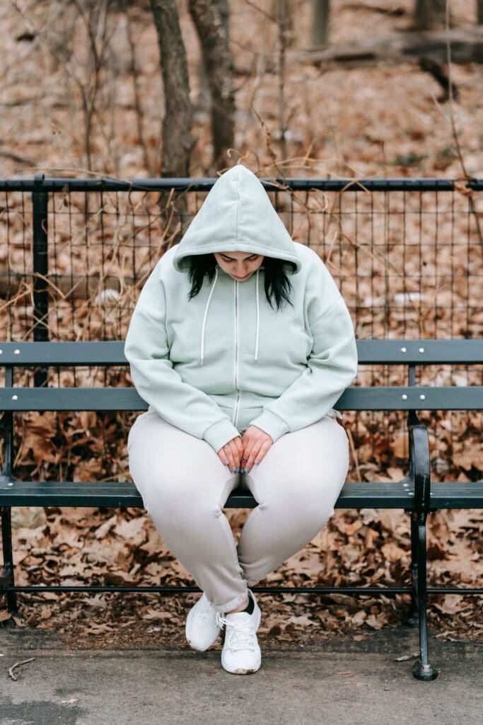 Woman sitting alone on a park bench in autumn, reflecting on emotional pain and the roots of self-medicating