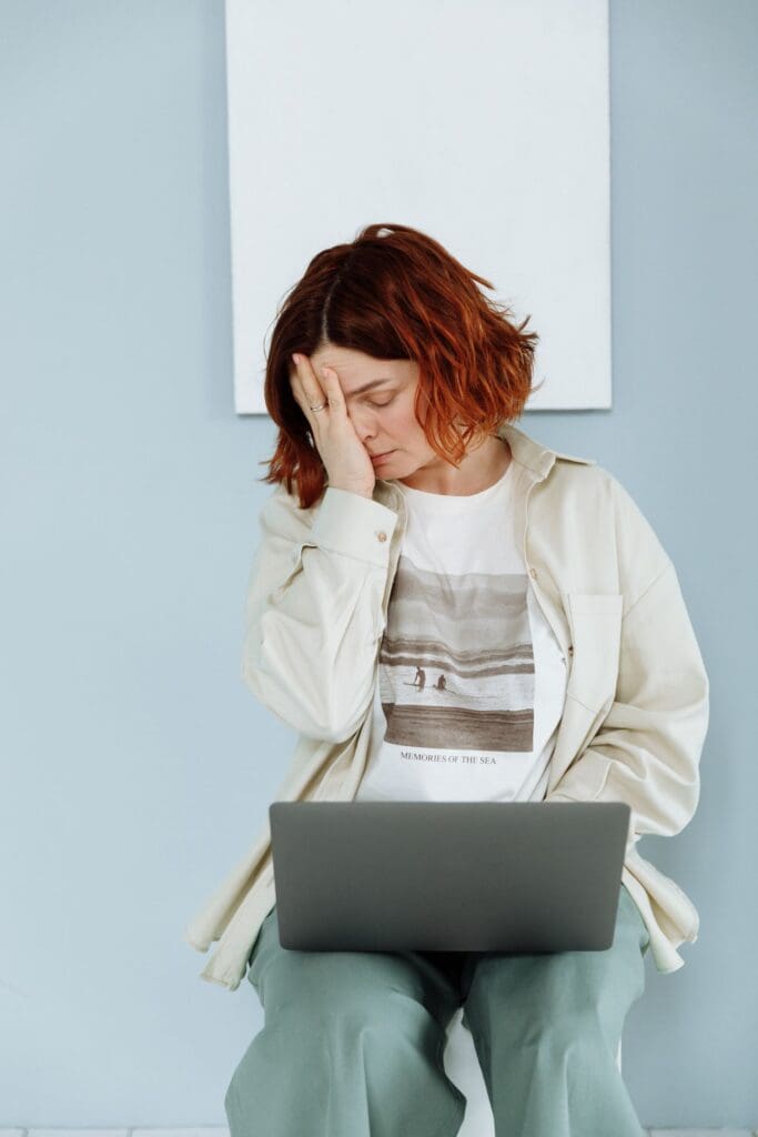 Exhausted woman sitting with a laptop, head resting on her hand, showing signs of burnout and emotional fatigue