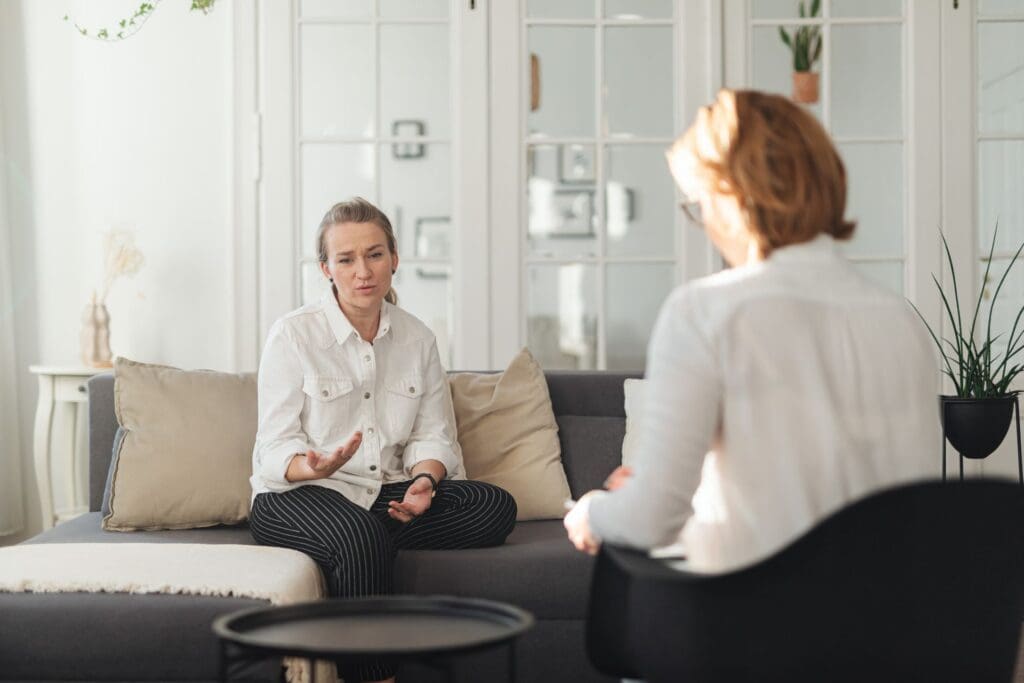 Woman sitting on a couch and speaking openly during a therapy session with a female therapist in a calm, bright office