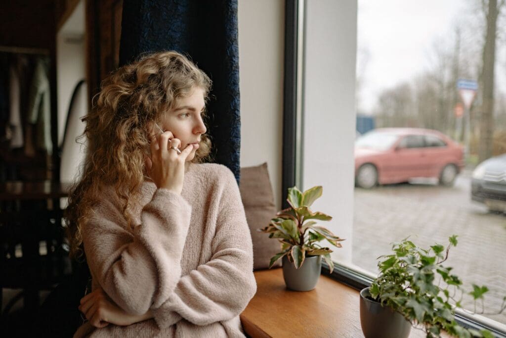 Worried woman on a phone call, looking out a window, absorbed in someone else’s situation.