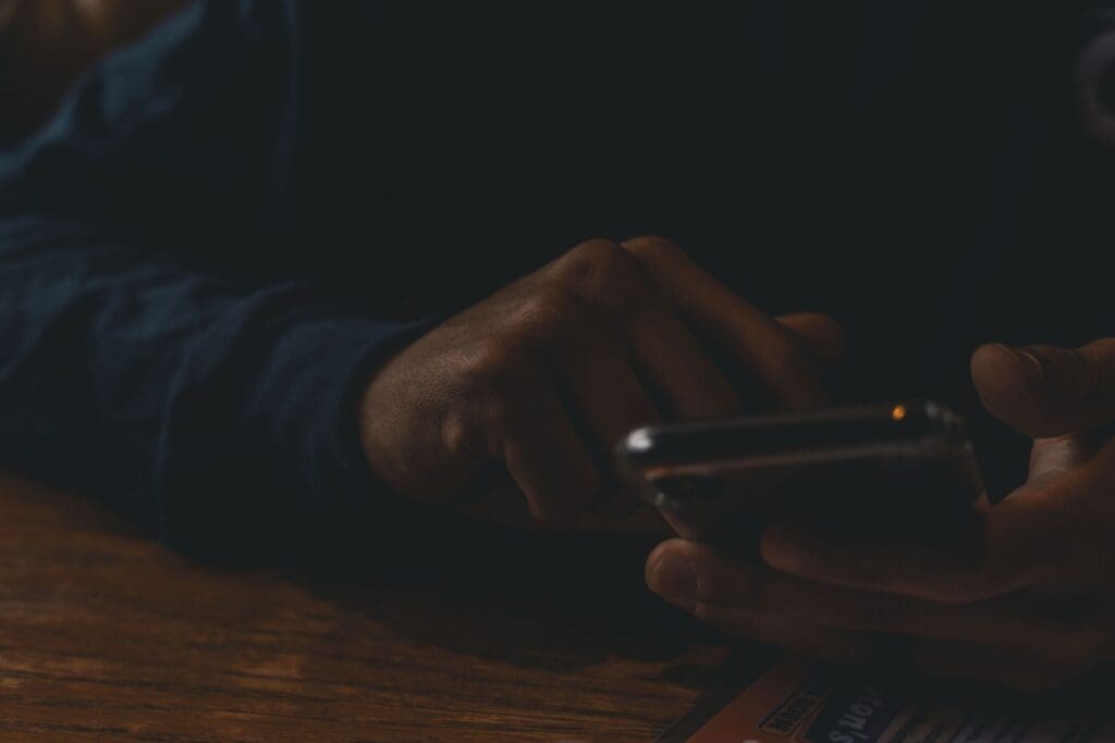 Hands holding a smartphone in a dark room, scrolling late at night.